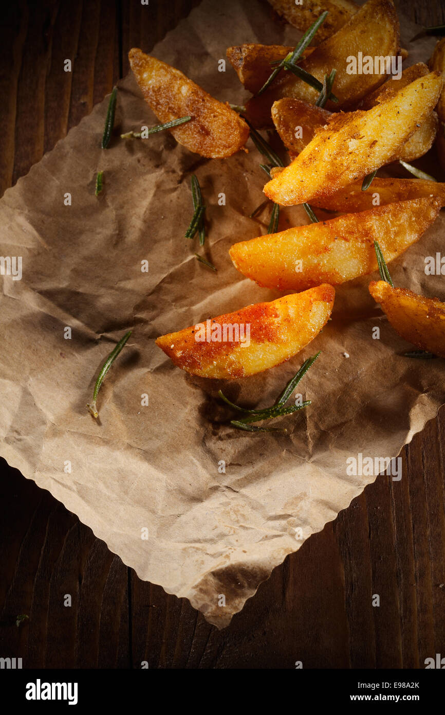 Würzige Ofen gebacken oder gebratene Kartoffelspalten mit frischem Rosmarin auf einem Blatt Grunge braun Stockfoto