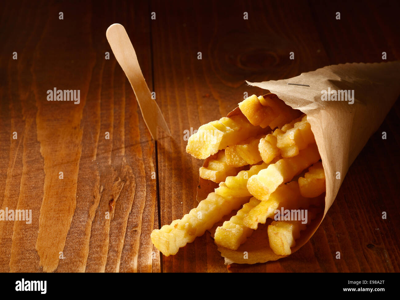 Crinkle cut goldene Pommes frites diente als ein Imbiss in einer Papierrolle braun liegend auf einem Holztisch mit Exemplar Stockfoto