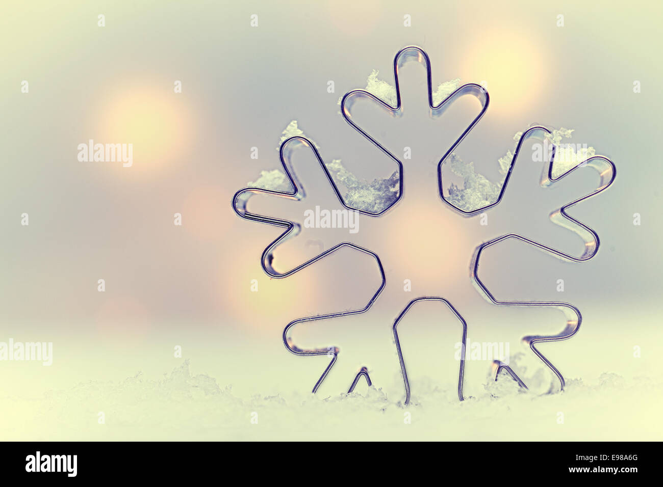 Ätherisch Schneeflocke saisonalen Hintergrund mit einer Schneeflocke-förmigen Metall Cookie Cutter Oulined gegen weich gedämpft Weihnachtsbeleuchtung mit copysapce Stockfoto