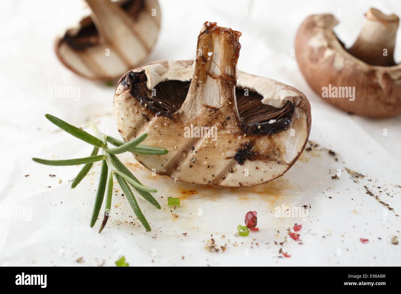 Frisch gegrillte halbierte Pilze, gewürzt mit Pfeffer und ein Zweig frischer Rosmarin für eine gesunde vegetarische Gericht Stockfoto