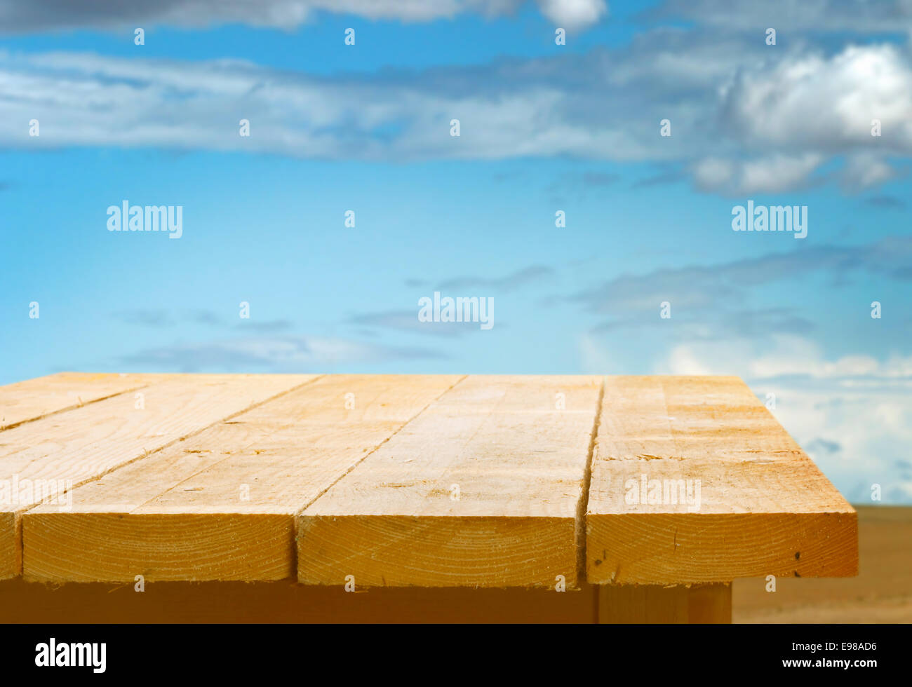 Leere hölzerne Tischplatte vor blauem Himmel mit flauschigen weißen Wolken für die Platzierung Ihrer Nahrung oder Produkt Stockfoto