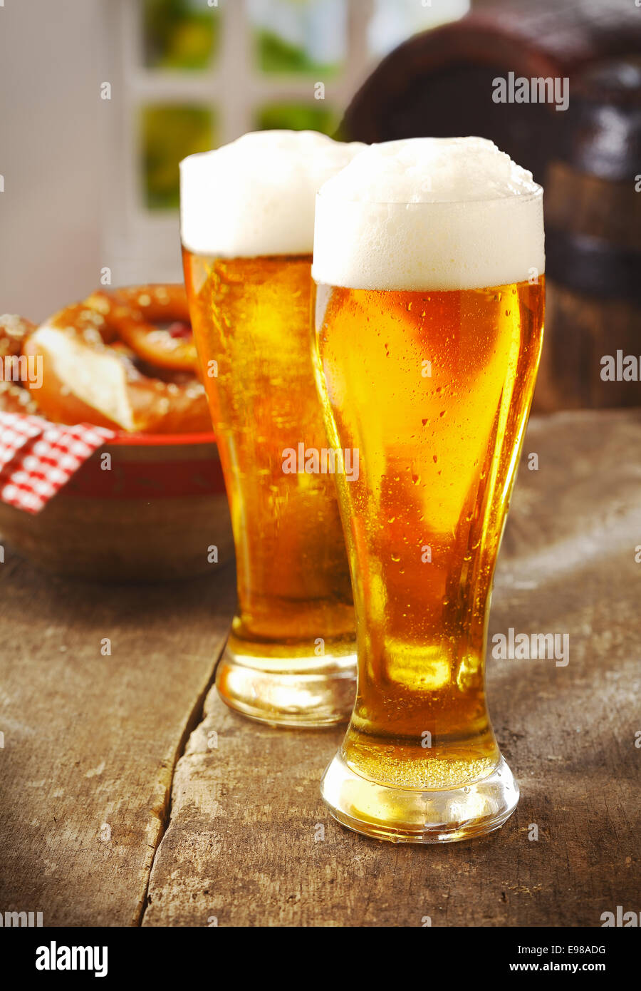 Zwei große Gläser golden Ale oder Bier mit einem guten Kopf des weißen Schaum auf einem alten hölzernen Küchentisch mit einem Korb mit Brötchen hinter Stockfoto