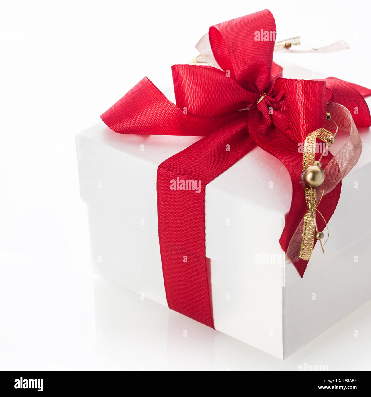 Dekorative rote Schleife mit einem goldenen Quaste und Christbaumkugel Highlight auf einer weißen Geschenkbox für feiern Weihnachten, Valentinstag, Geburtstag oder ein Jubiläum auf einem weißen Hintergrund Stockfoto
