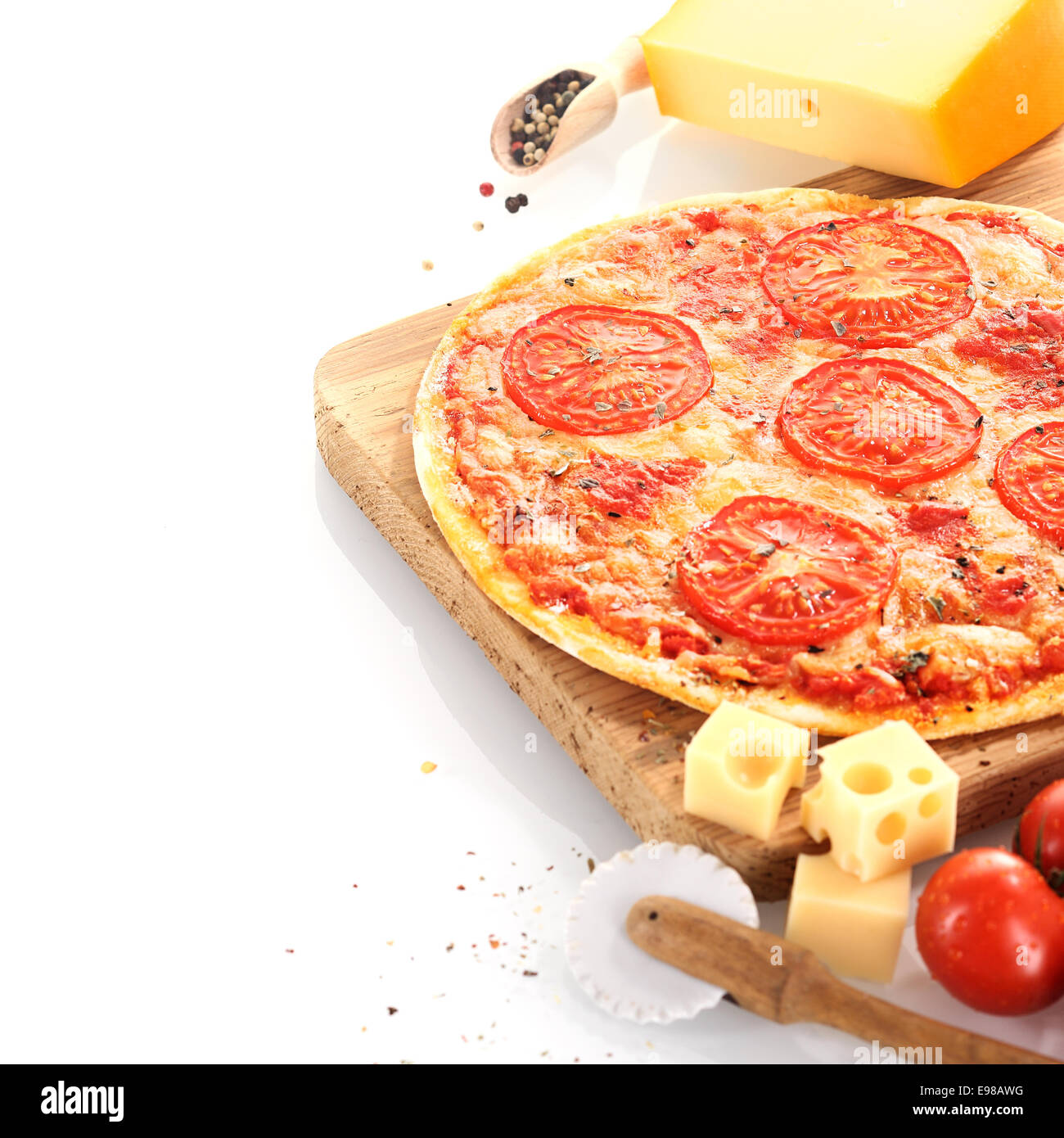 Hausgemachtes Käse und Tomaten Pizza umgeben von frischen Zutaten und einer Pizza-Rad und serviert auf einem Holzbrett über weiß Stockfoto