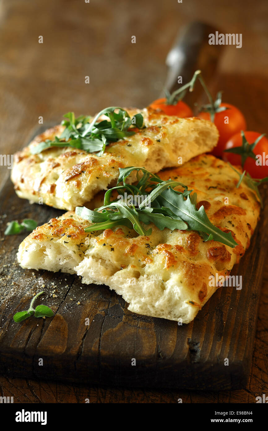 Herzhaft überbackene italienische Focaccia Brot garniert mit Blätter Rucola auf eine alte Vintage Holz Küchentisch Stockfoto