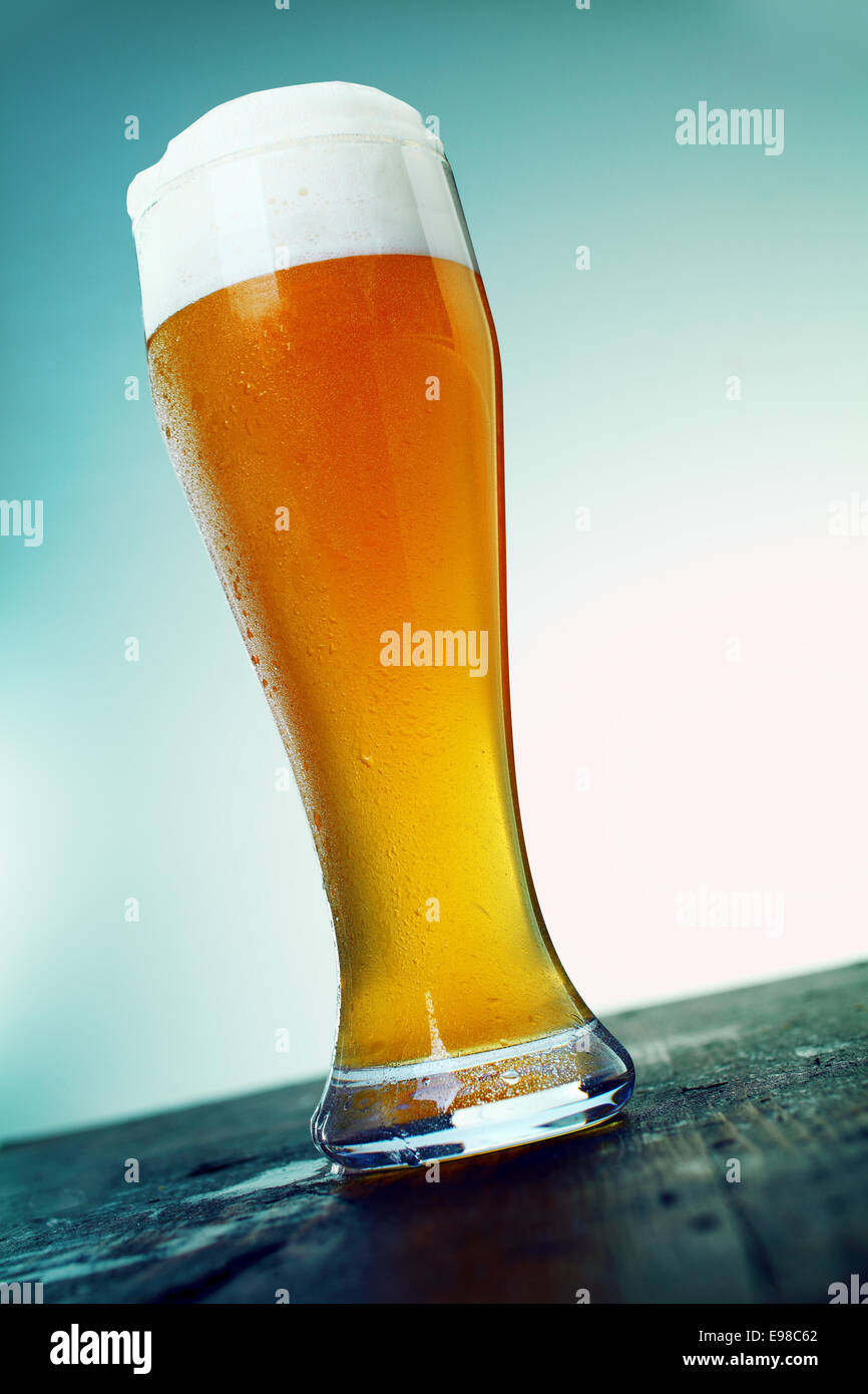 Langen kalten Pint Bier in einem eleganten Glas mit einem guten Kopf von Schaum auf eine alte hölzerne Theke einer Bar oder Club, niedrigen Winkel Blick stehen. Schauen Sie sich mein Portfolio für eine ganze Reihe von Cocktails. Stockfoto