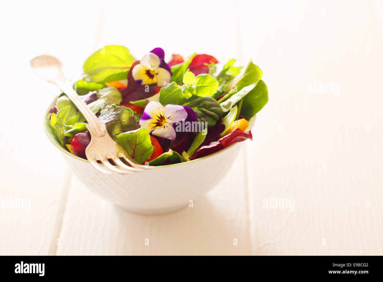 Gesunden Bauernhof frischer Kräutersalat mit Blattgemüse und Kapuzinerkresse Blüten in einer weißen Schüssel mit einer Gabel auf einem weißen Holztisch serviert Stockfoto