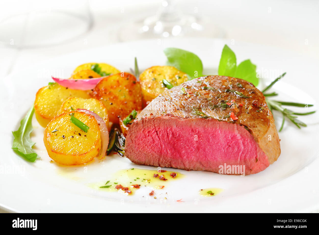 Durchschneiden Portion leckeren blutigen serviert mit knusprigen Bratkartoffeln, frischem Rosmarin und Rucola auf einem weißen Teller selten, mittlere seltene Filetsteak Stockfoto