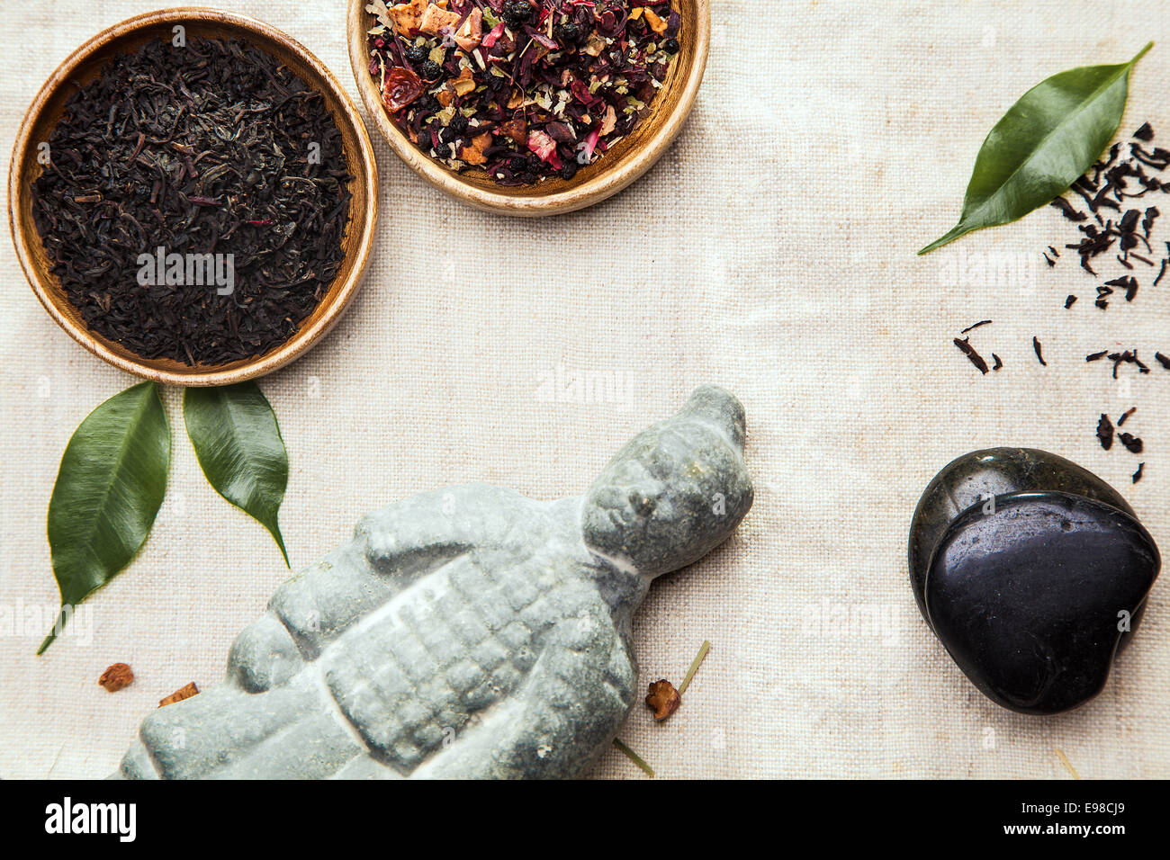 Kräuter-Tee-Blätter für alternative Therapie in zwei kleine Schüsseln mit einem asiatischen Statue und Spa massage Steinen auf einem leicht strukturiertem Textil-Hintergrund Stockfoto