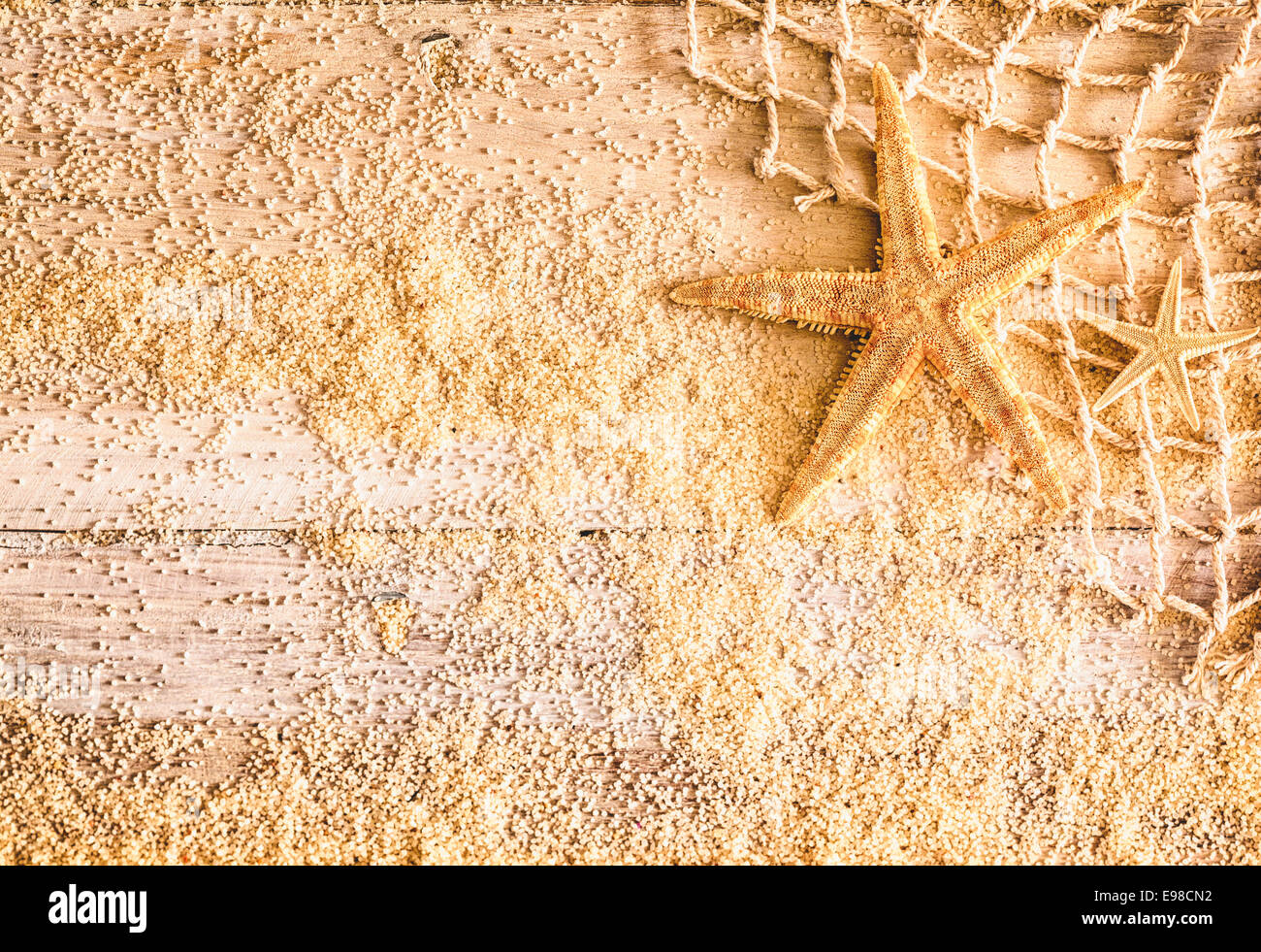 Erinnerungen an einen tropischen Sommerurlaub mit einem Seestern, Angeln net und verstreuten goldenen Strandsand auf urigen Holzbrettern mit Exemplar für einen ziemlich nautischen Hintergrund Stockfoto