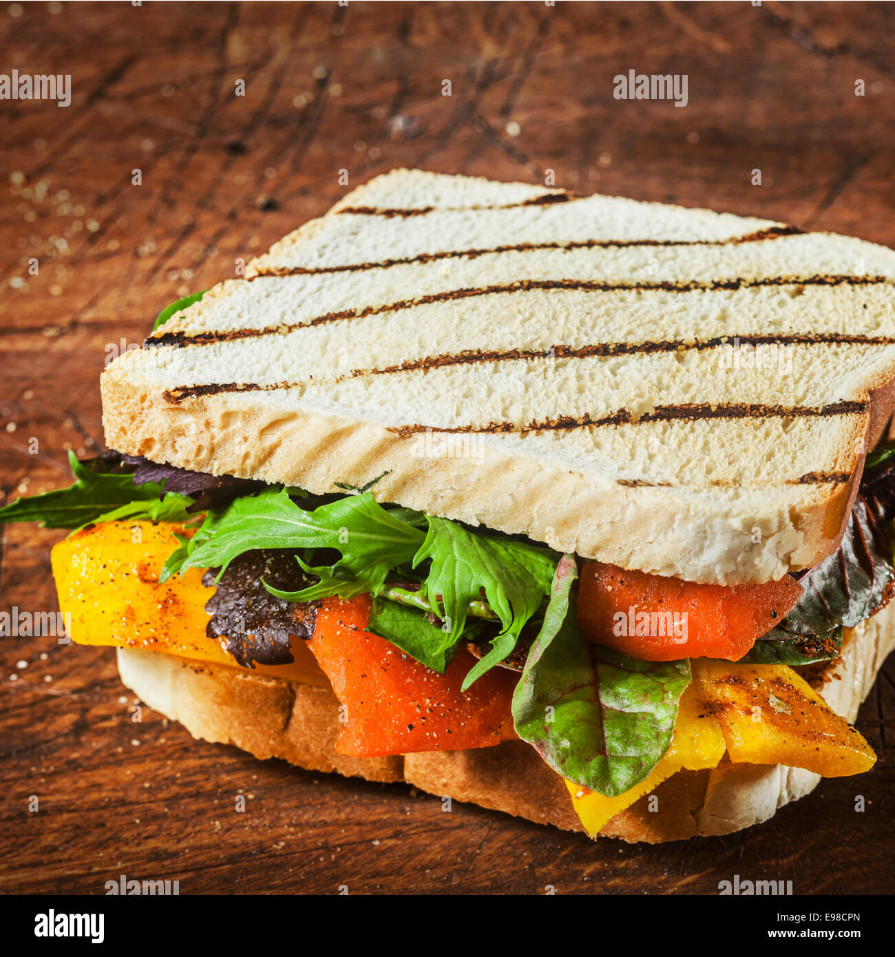 Leckere gegrillte Kräuter und Käse-Sandwich auf zwei Scheiben Brot mit Rucola und Spinat, Paprika und Tomaten auf einem rustikalen Holztisch für einen gesunden Mittagsimbiss, Nahaufnahme Stockfoto