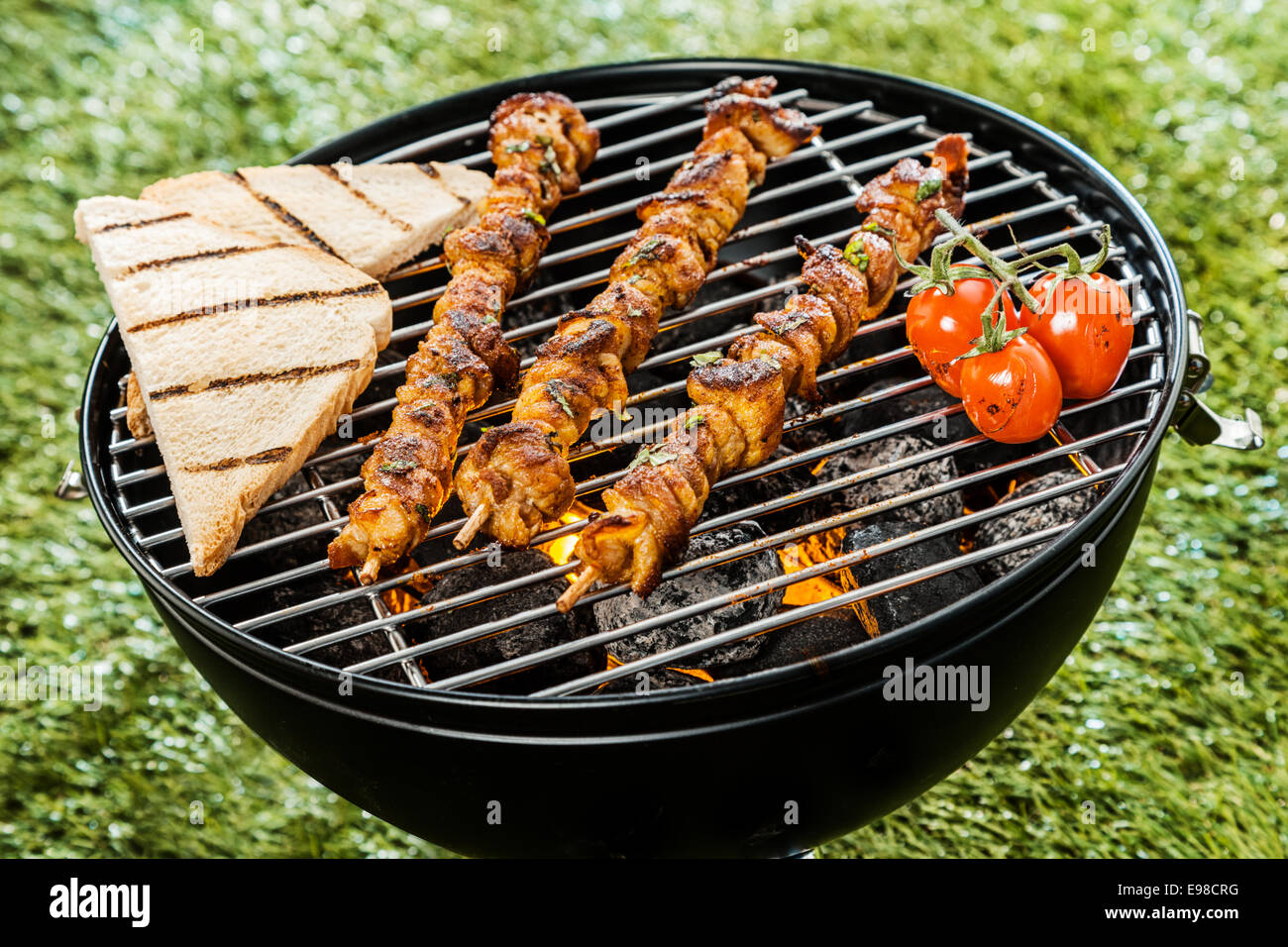 Drei köstliche Fleisch-Kebab Grillen auf einem BBQ-Feuer mit Scheiben Toast und Tomaten bei einem Sommerpicknick im Garten, Nahaufnahme hohen Winkel Stockfoto