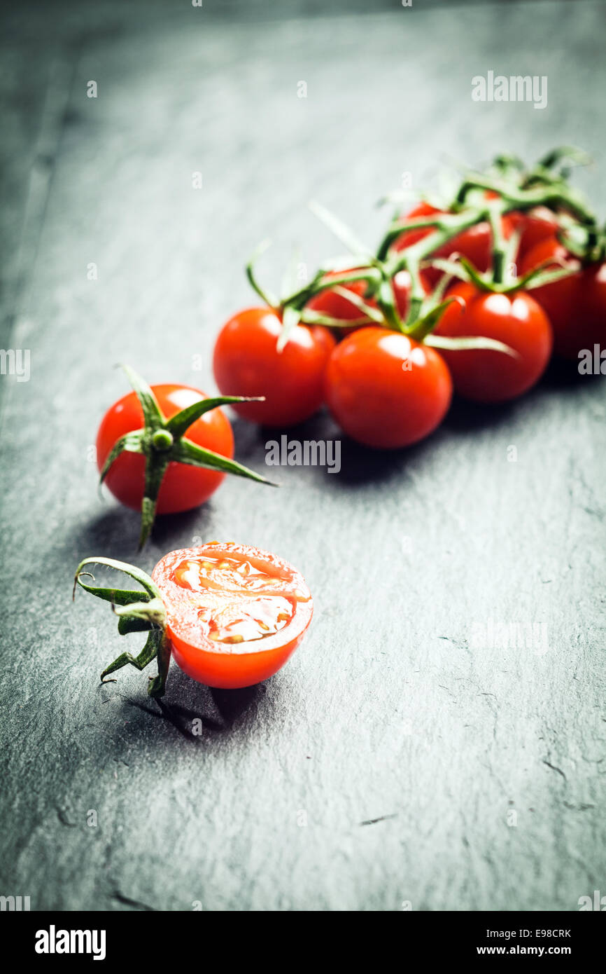 Traube Tomaten am Rebstock mit einer einzigen halbierte Tomate im Vordergrund auf eine strukturierte Oberfläche mit Highlight und Exemplar und Stockfoto