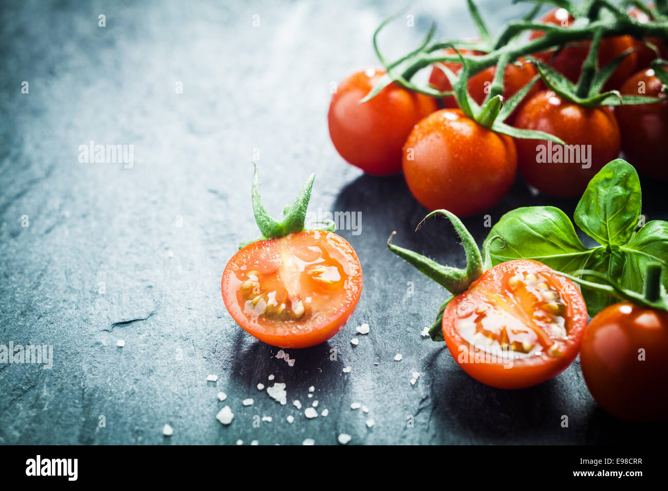 Frische Trauben Tomaten mit Basilikum und grobes Salz für den Einsatz als kochen Zutaten mit halbierten Tomaten im Vordergrund mit Exemplar Stockfoto