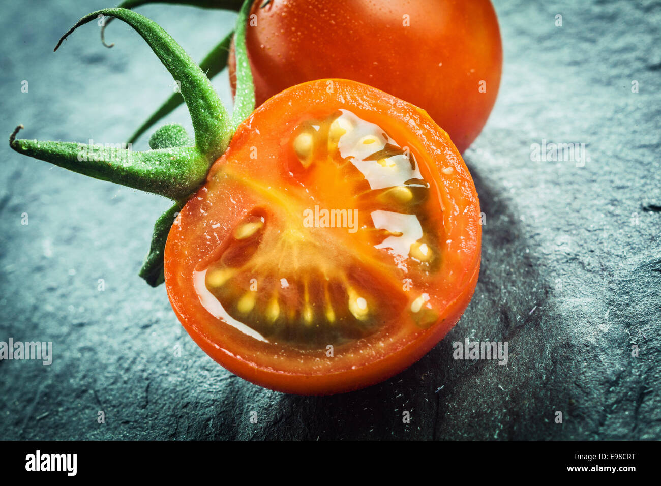 Nahaufnahme einer halbierten saftig frische Trauben Tomate zeigt die Kerne und das Fruchtfleisch mit einem grünen Stiel für einen gesunden Salat oder Kochzutat Stockfoto