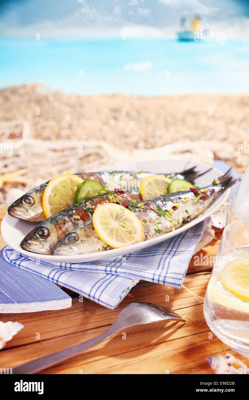 Ganze garniert Pfanne gebratenen Fisch serviert am Strand auf einer ovalen Platte garniert mit Zitrone und genießen Sie einen tropischen Sommerurlaub Stockfoto