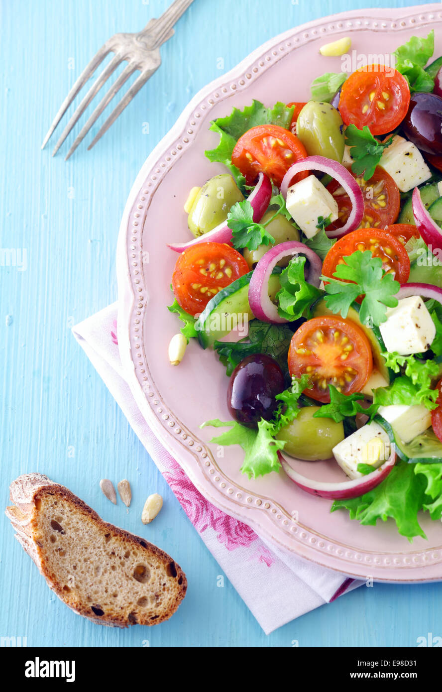 Draufsicht auf eine Portion Feta-Käse-Salat mit Oliven und Kirschtomaten auf einem erhabenen weißen Teller mit einer Scheibe Roggenbrot Stockfoto