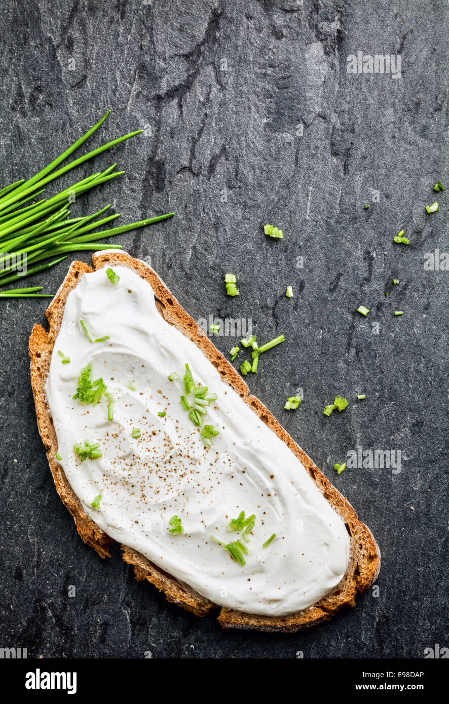 Frischkäse mit Schnittlauch auf einer Scheibe gesundes Roggenbrot mit frischem Schnittlauch auf eine dunkle Textur von oben gesehen Stockfoto