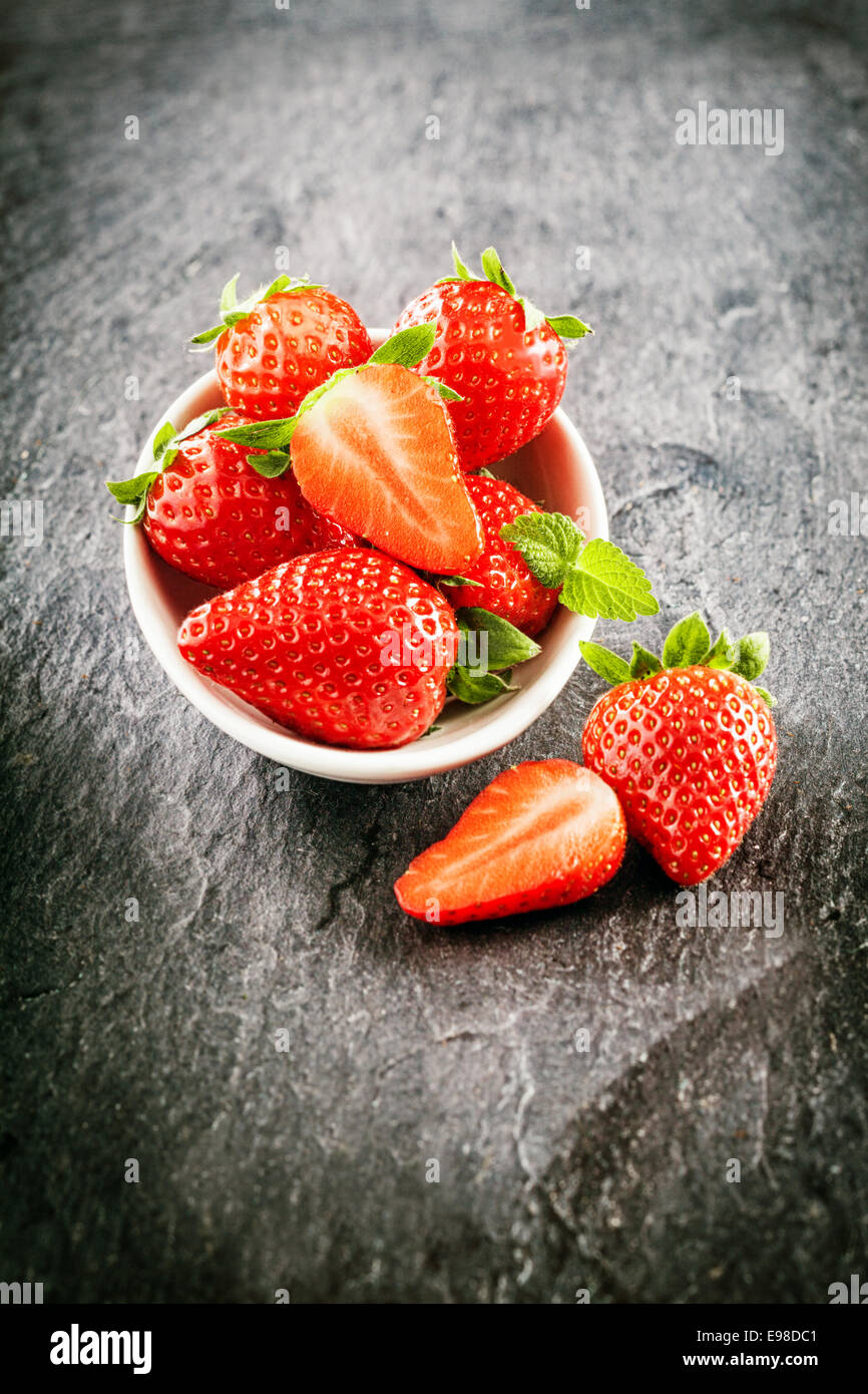 Köstliche Bauernhof frischen saftigen Erdbeeren serviert in einer Schüssel mit ganze und halbierte Früchte in einer hohen Winkel Ansicht auf dunklen Schiefer mit Vignettierung Stockfoto