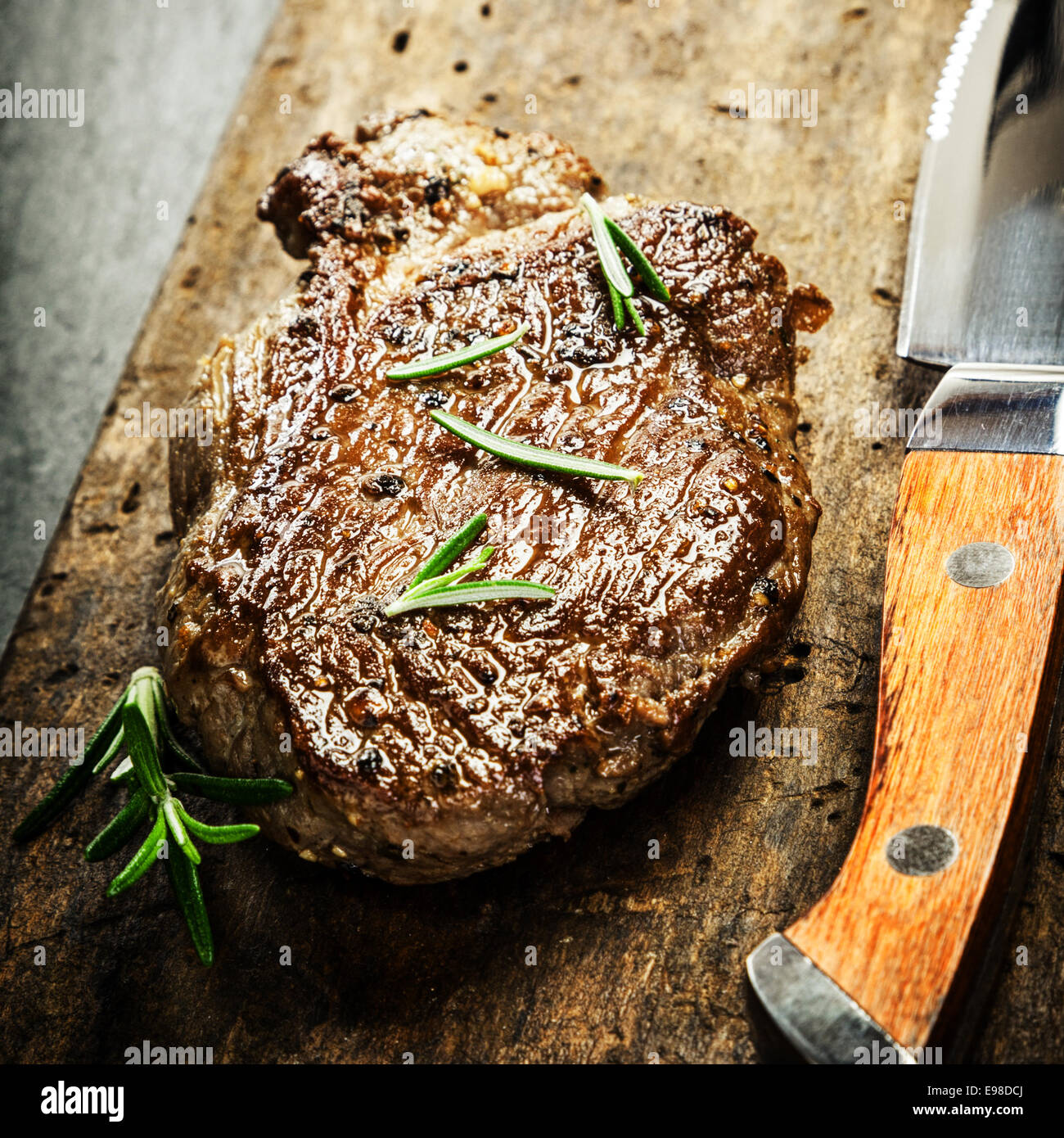 Saftige Portion gegrilltes Rindersteak, garniert mit frischem Rosmarin auf eine rustikale Schneidbrett aus Holz mit einem Steak-Messer für ein Gourmet-Menü Stockfoto