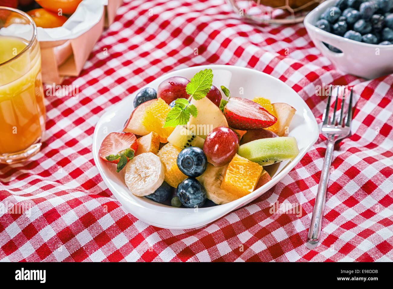 Gesunde Sommer-Picknick mit bunten tropischen Obstsalat serviert in einer Schale auf einem roten und weißen aufgegebenes Tuch Stockfoto