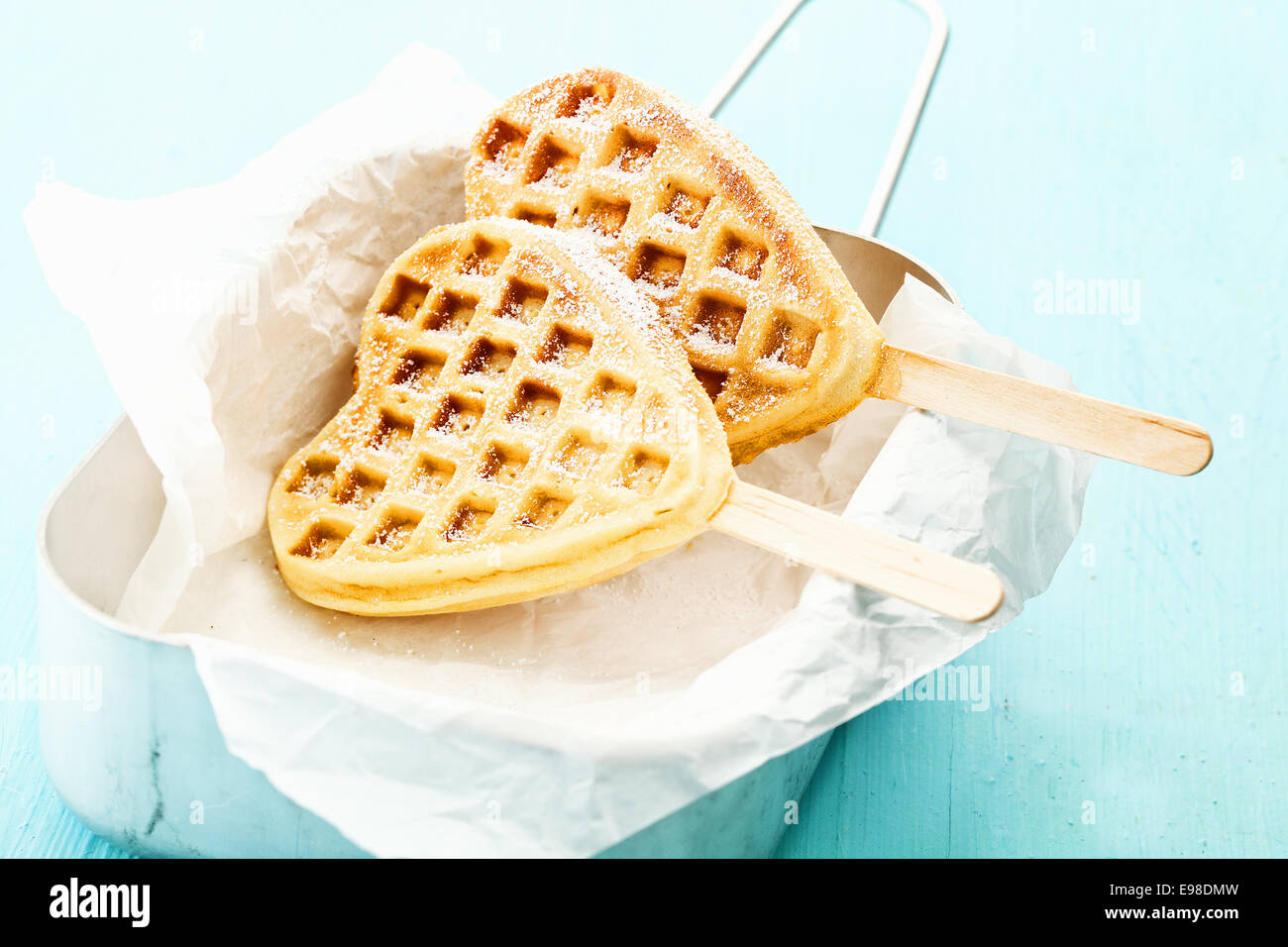 Zwei herzförmige Waffeln am Stiel in einer Blechdose eine ein Papier wickeln, mit Zucker und Zimt bestreut Stockfoto