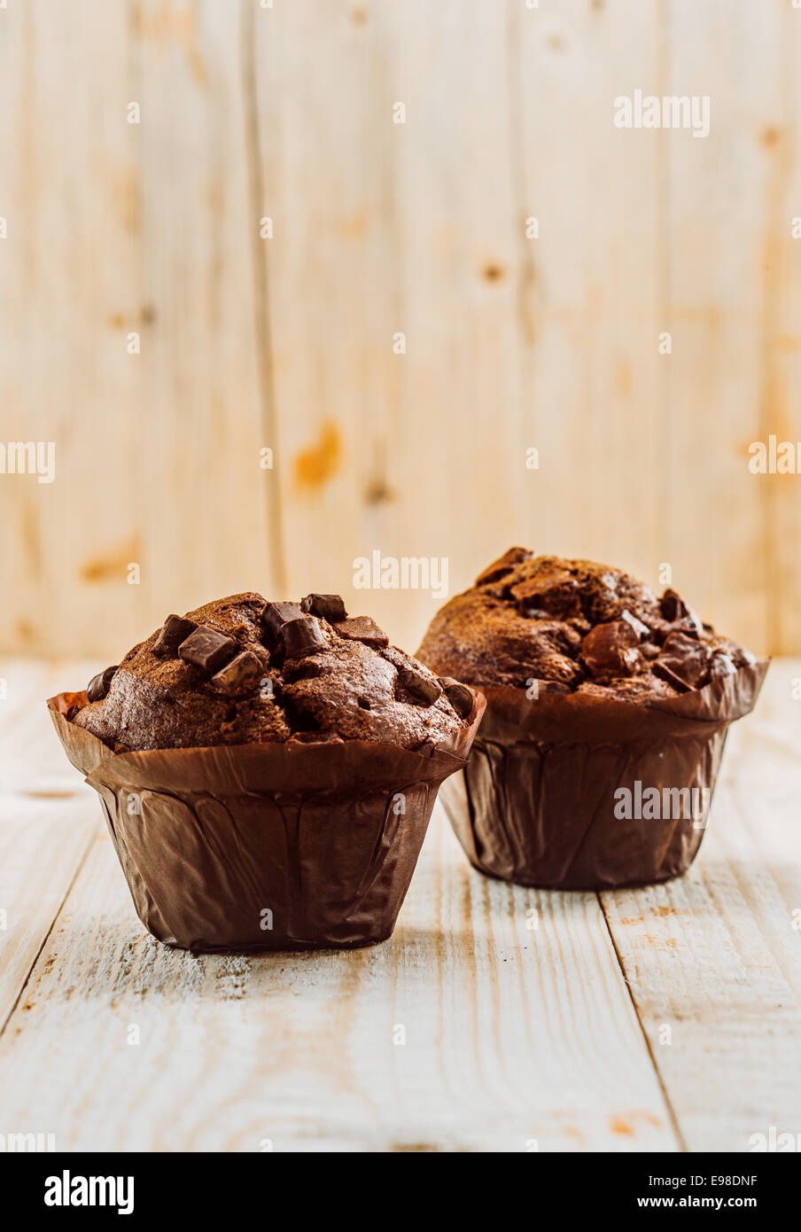 Zwei gebackene frisch lecker chocolate Chip Muffins in braunem Papier, die Tassen auf einer hölzernen Tischplatte in eine rustikale Küche mit einer Holzmaserung stehend zu beenden und Exemplar Stockfoto