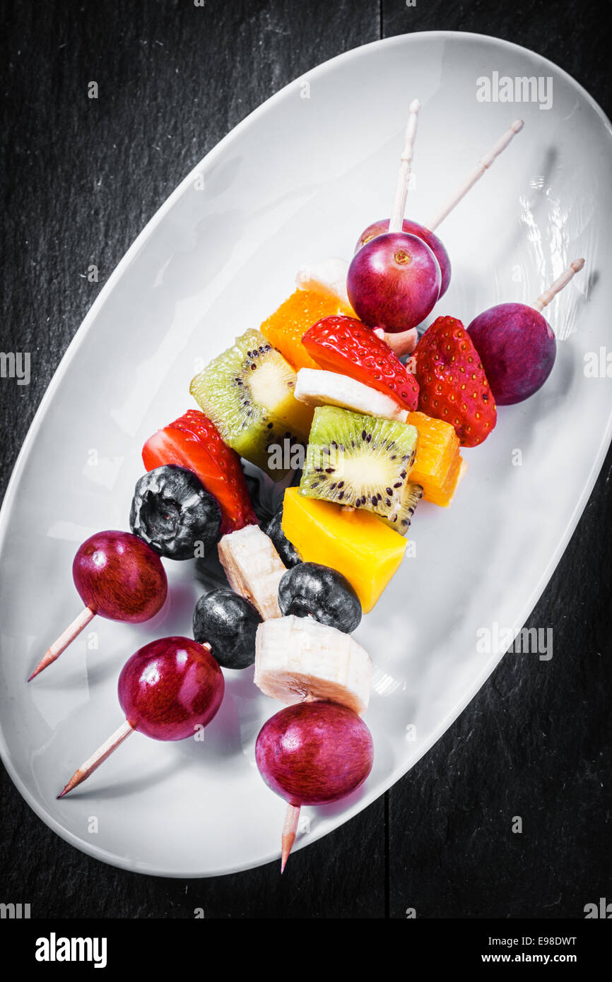 Obenliegende Nahaufnahme von lecker gesundes Obst Kebab mit Erdbeeren, Heidelbeeren und tropische Früchte wie Kiwis, Stockfoto