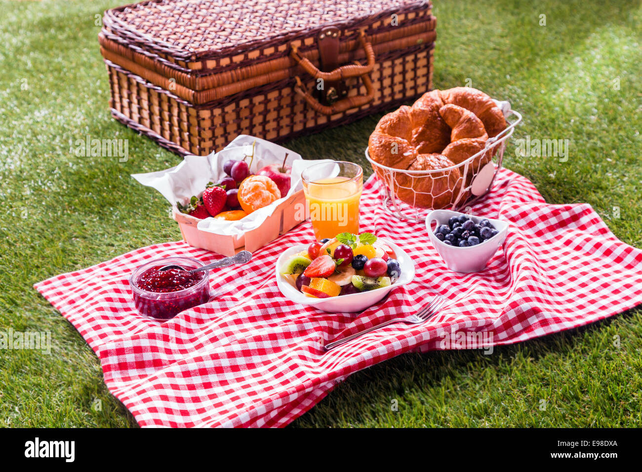 Bunte gesunde Sommer-Picknick ausgebreitet auf einem roten und weißen aufgegebenes Tuch neben einen geflochtenen Korb mit frischen Früchten und Obst Stockfoto