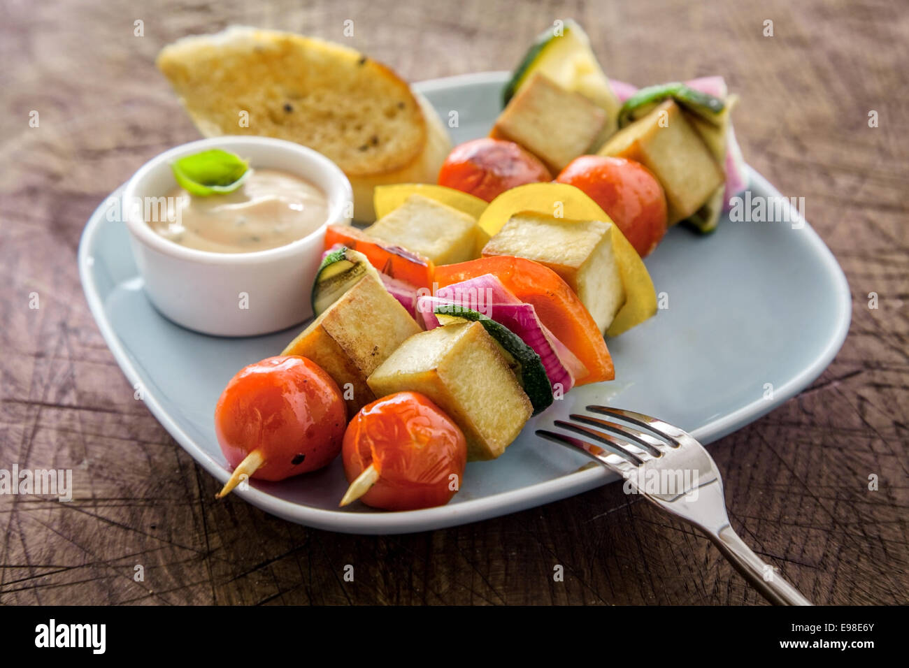 Gegrillter Halloumi und Gemüse Kebab serviert auf einem Teller mit einer Schüssel mit pikante Sauce und golden knusprig geröstetem Baguette auf einem Grunge Holz Picknick-Tisch Stockfoto