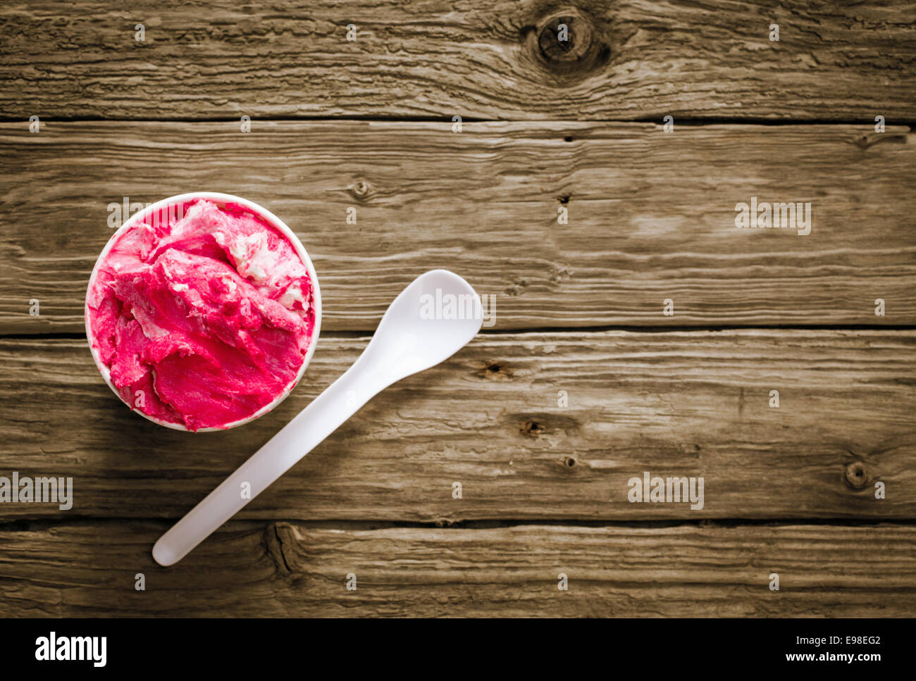 Appetitlich Wanne mit hell rosa Beeren-Eis auf einem rustikalen Holztisch mit einem Einweg-Plastik Löffel für einen erfrischenden Sommer-snack Stockfoto