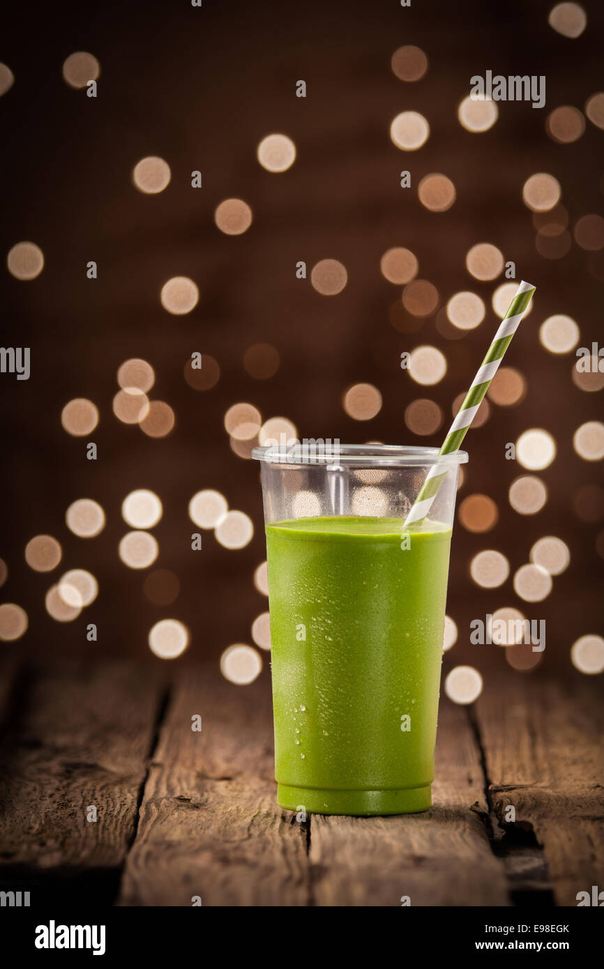 Glas gesunde grüne Gemüse Smoothie, stehend auf einem rustikalen Restauranttisch mit einem Bokeh Party Lichter im Hintergrund Stockfoto