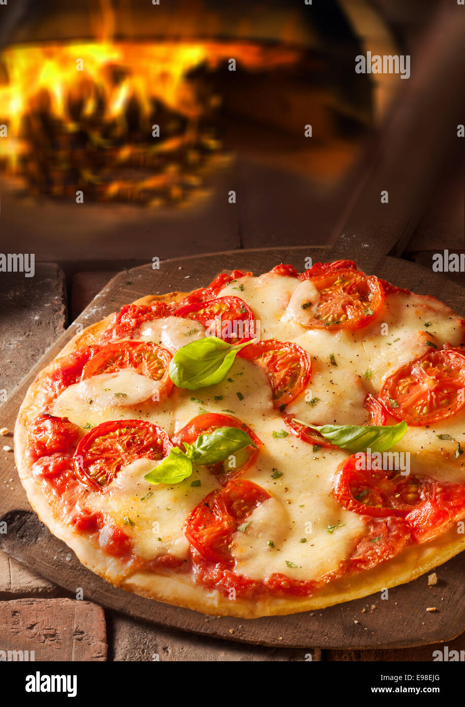 Leckere italienische Pizza mit geschmolzenem Käse und Tomaten in einer Pizzeria mit dem Feuer aus dem Ofen sichtbar hinter Stockfoto