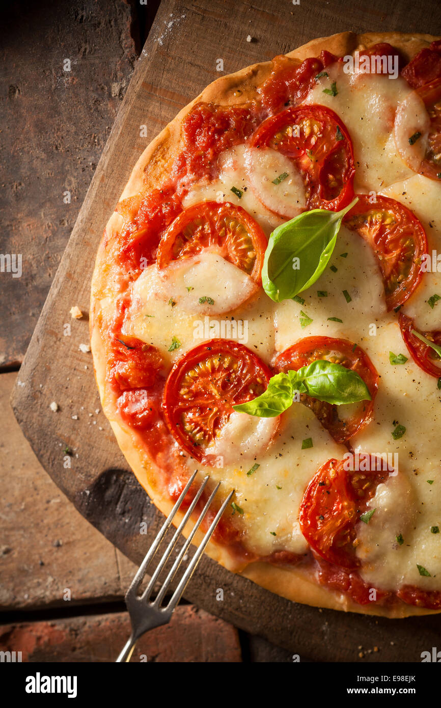 Draufsicht auf eine schmackhafte Tomaten Pizza mit goldenen geschmolzenem Käse und Basilikum serviert auf einem alten Holzbrett Stockfoto