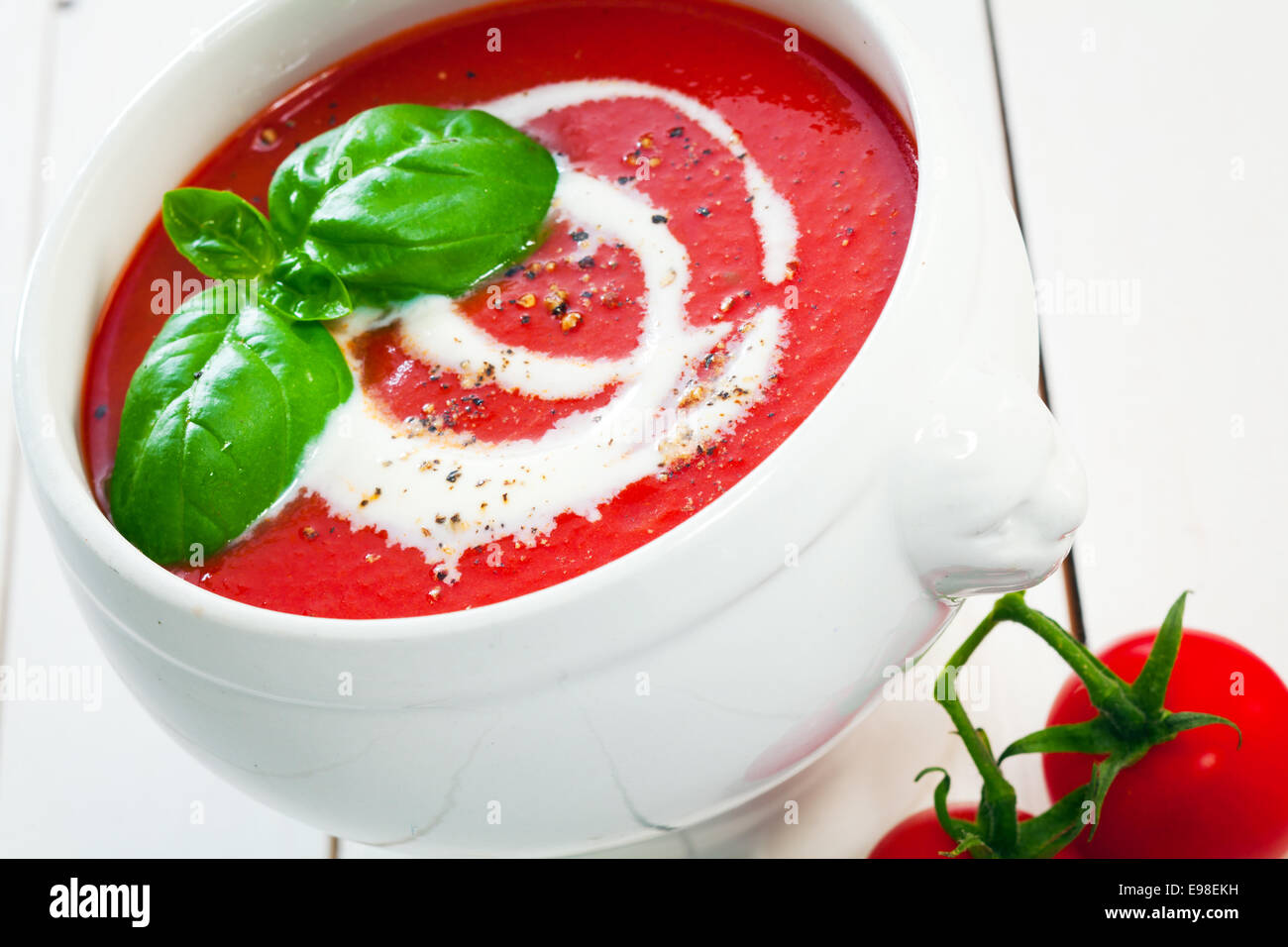 Nahaufnahme der geneigten Winkel einer Schüssel bunten roten frische Tomatensuppe mit Sahne beträufelt und mit Basilikum garniert Stockfoto