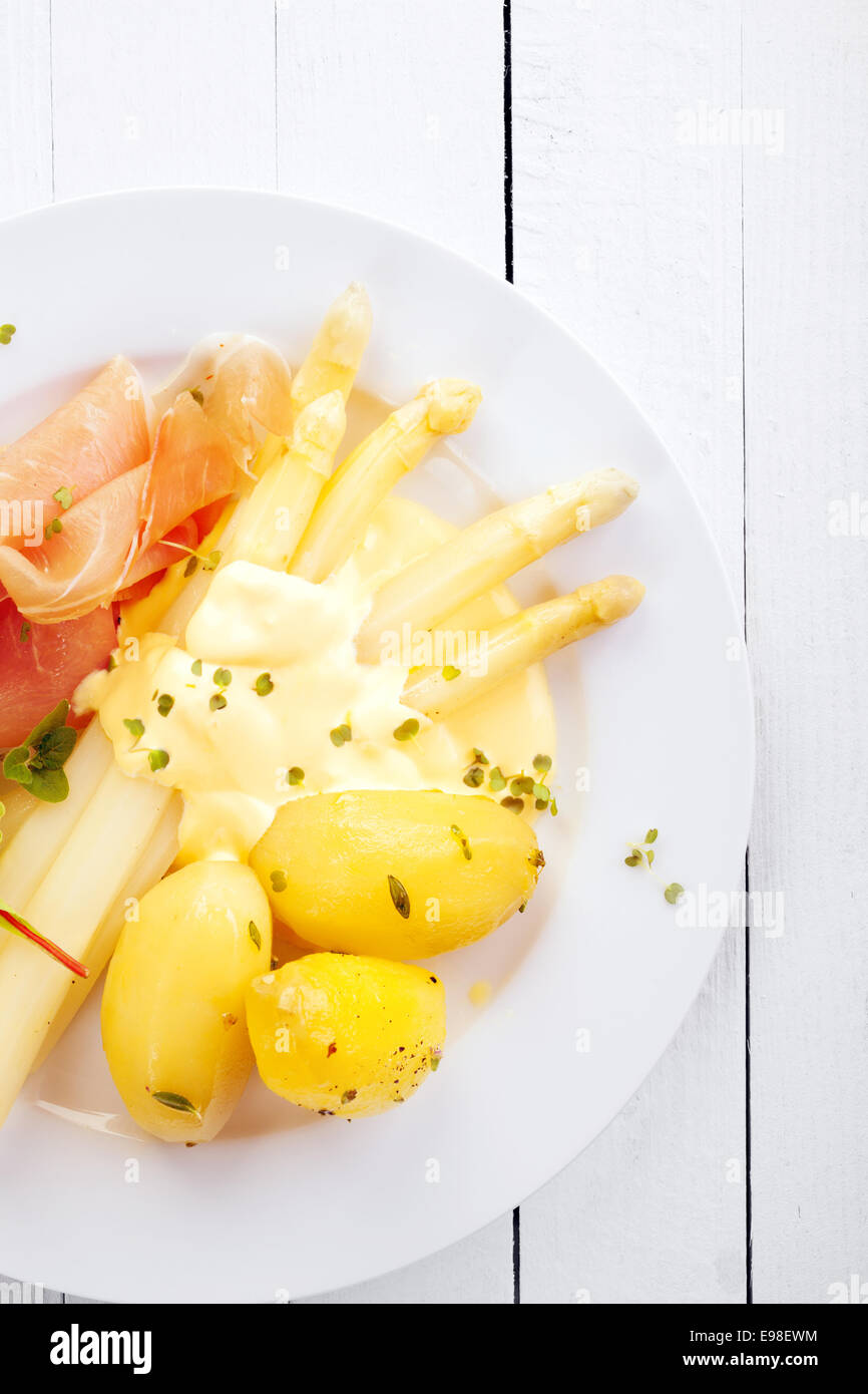 Herzhafte Mahlzeit mit Spargel und dünn geschnittenen Schinken mit Baby gekochte Kartoffeln und Mayo-Sauce auf einem weißen Teller auf weiß bemalten Holztafeln, Closeup von oben gesehen Stockfoto