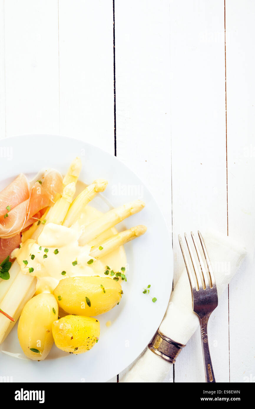 Weißer Spargel mit Schinken und Baby gekochte Kartoffeln garniert mit cremigen Mayonnaise serviert auf einem weißen rustikale lackierten Holztisch mit Exemplar Stockfoto