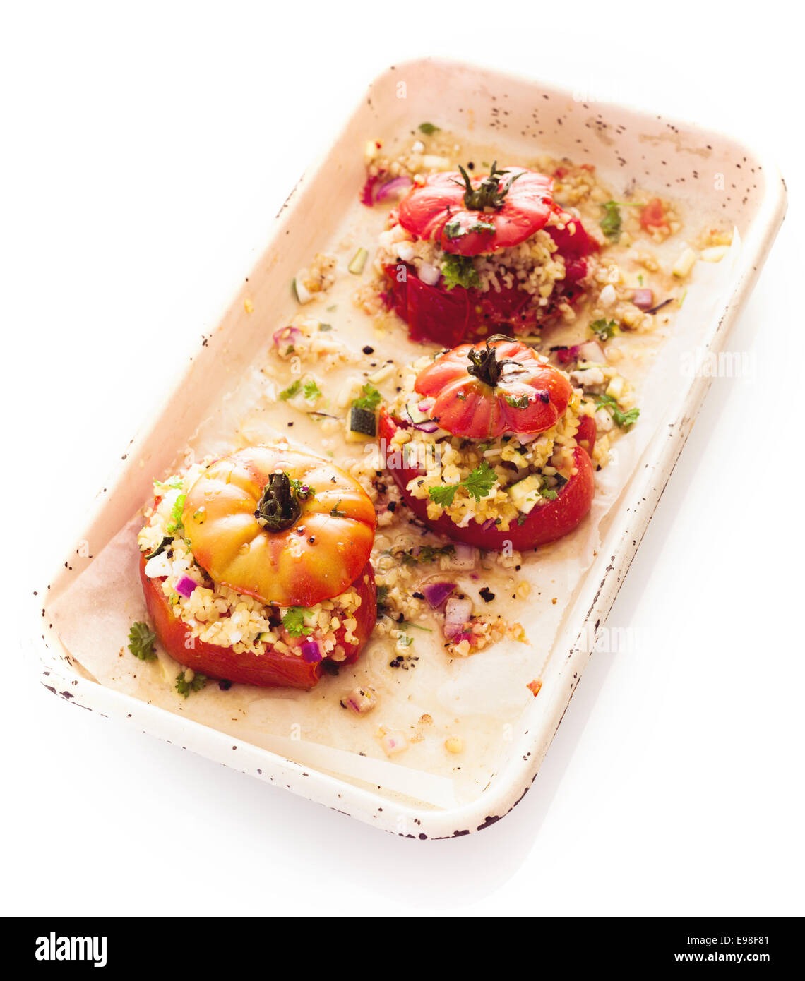 Portion gesunde vegetarische Küche mit einem Teller gefüllte Reife rote Gebackene Tomaten mit Couscous, Zwiebel und Kräutern auf weißem Hintergrund Stockfoto