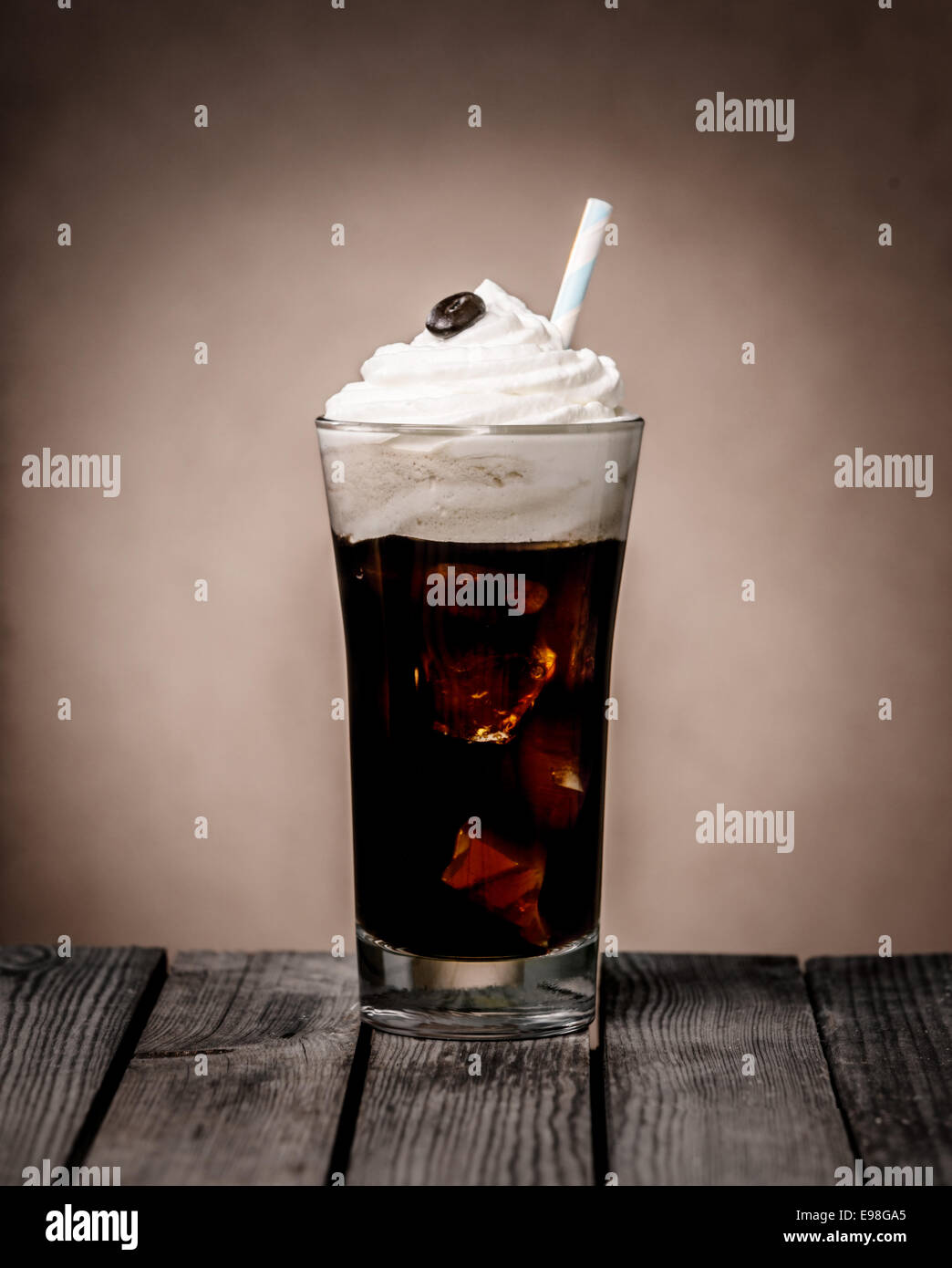 Großes Glas Eiskaffee Float garniert mit ein Wirbel von cremiger Vanille-Eis und einer einzigen Kaffeebohne stehend auf einer rustikalen alten hölzernen Theke in einem Café oder Kaffee Haus Stockfoto