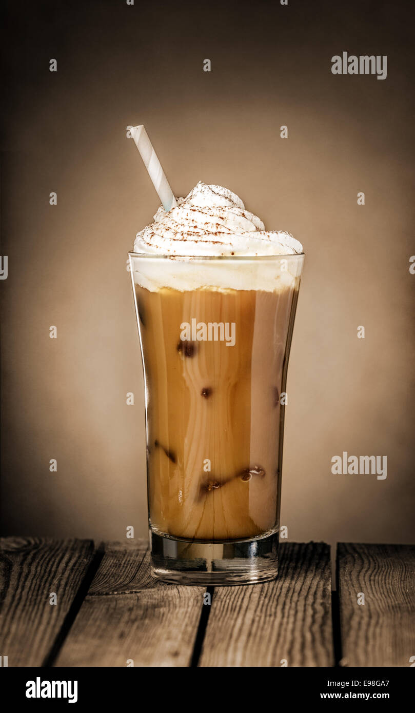 Großes Glas köstlichen kalten Eiskaffee Float oder Milchshake garniert mit Eis oder Sahne auf einer rustikalen hölzernen Theke für ein erfrischendes Sommer-Genuss Stockfoto