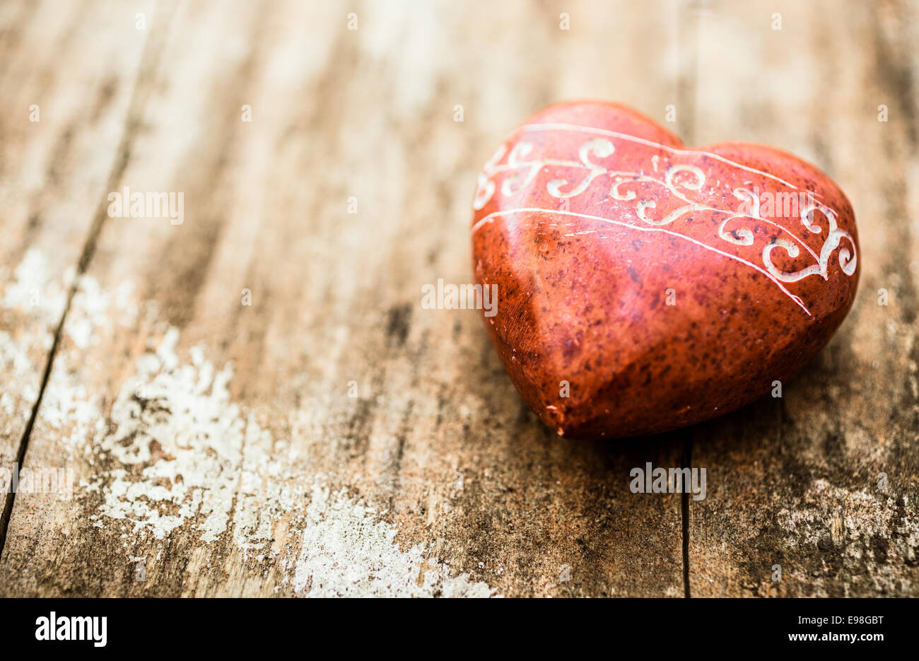 Roten Stein geformt wie ein Herz mit Schnitzereien auf eine Holzoberfläche. Stockfoto