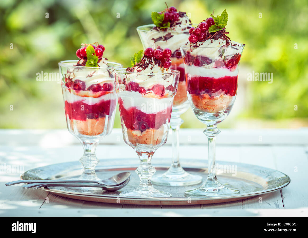 Köstliche Johannisbeer Eisbecher oder Desserts serviert im Freien auf Tablett mit große Gläser bunt geschichteten Beeren Coulis, Eis oder gefrorenen Joghurt, Sahne und Reife rote Johannisbeeren auf einem Kuchen Basis Stockfoto