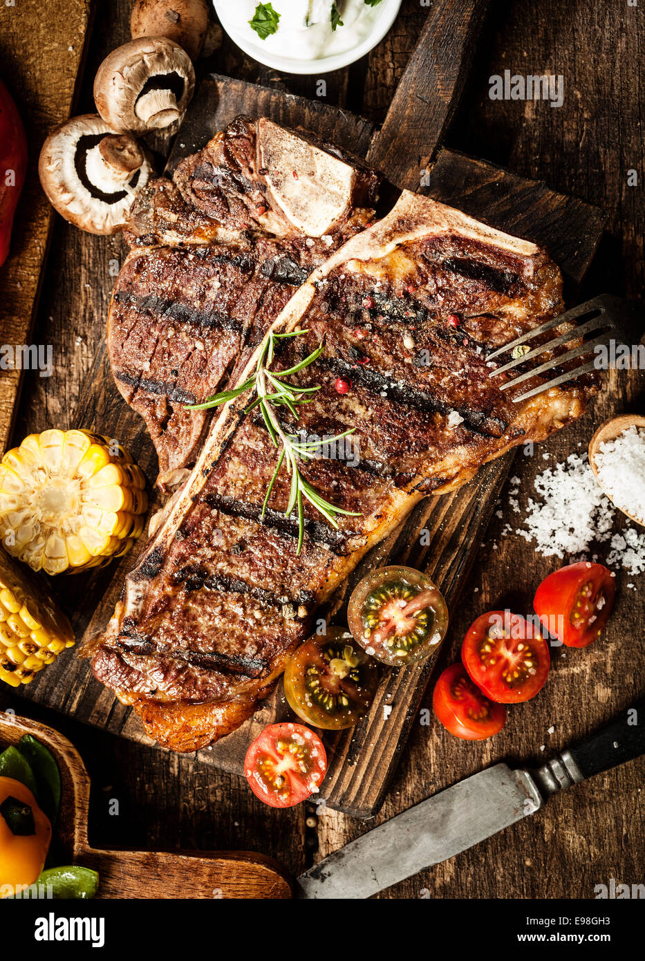 Gegrilltes t-Bone und Porterhouse-Steak, gewürzt mit Rosmarin in einer rustikalen Küche auf einem Holzbrett mit Tomaten, Mais, Pilze Stockfoto