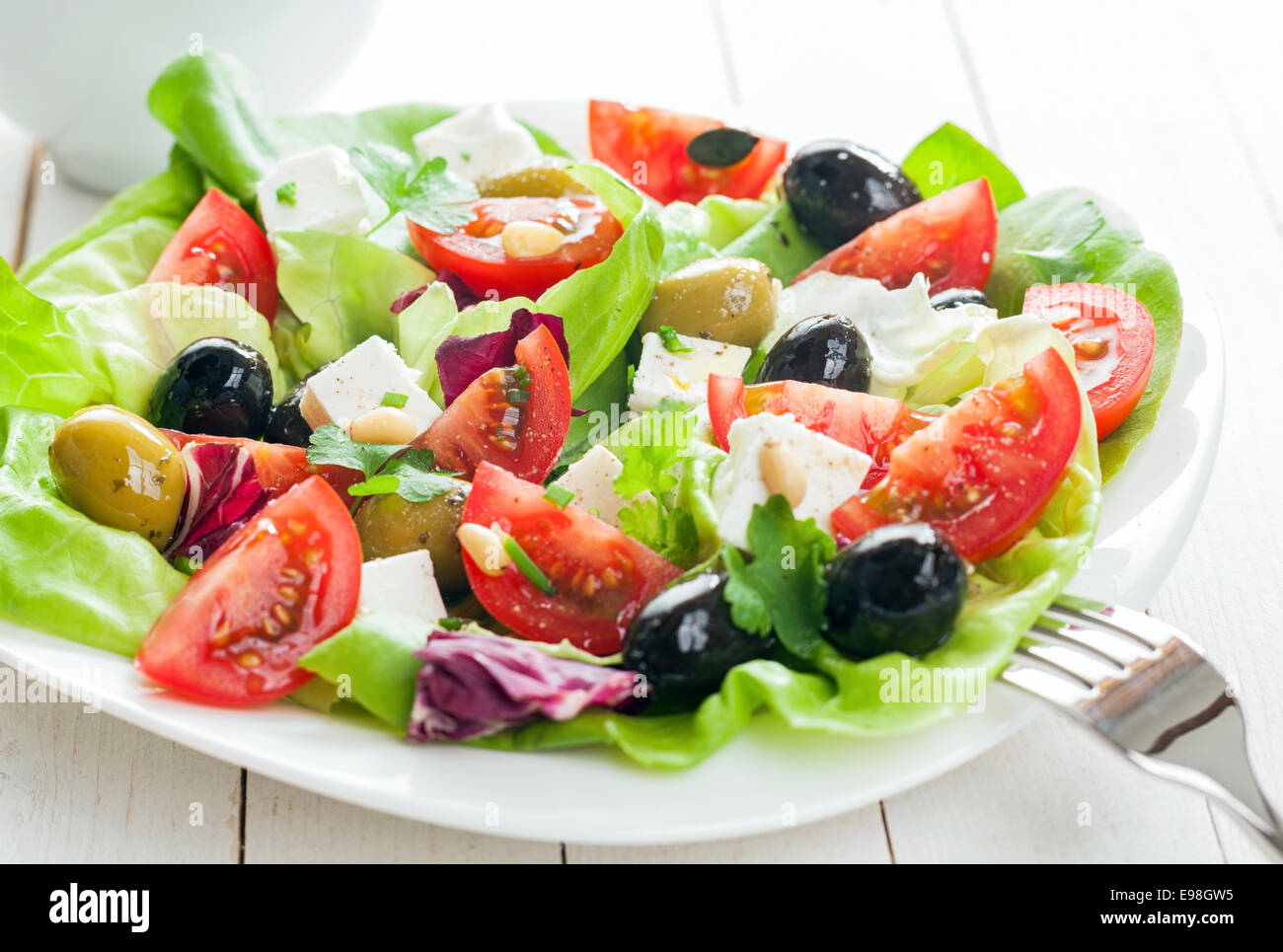 Teller mit frischen Salat mit Feta-Käse, Tomaten, Blattgemüse und gemischte Oliven auf rustikalen hölzernen Tafeln Stockfoto