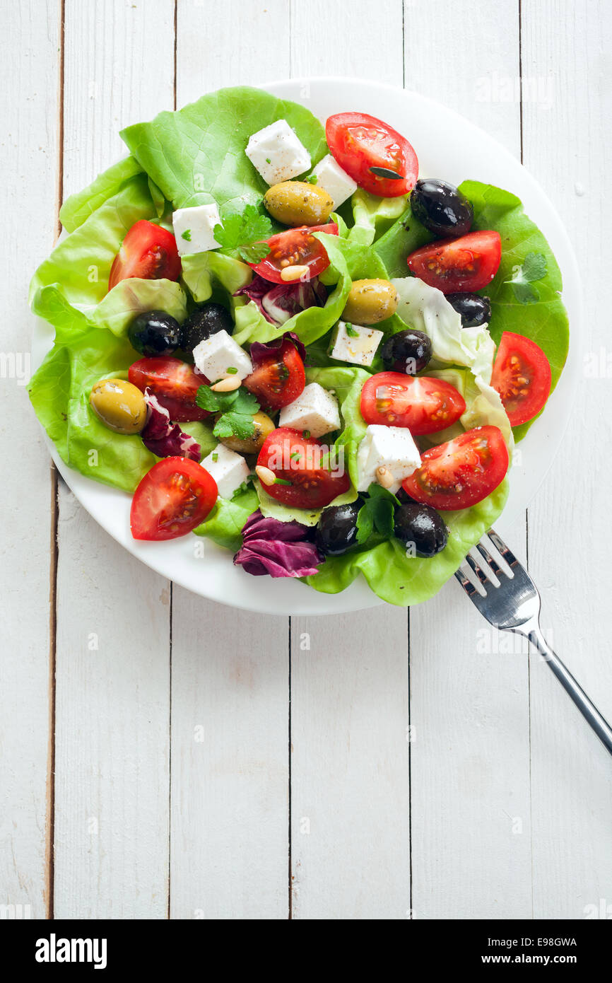Nahrhafter frischer Salat mit Feta, Tomaten, Blattgemüse und Oliven auf einer Platte, Draufsicht auf rustikalen bemalten Tafeln mit Stockfoto