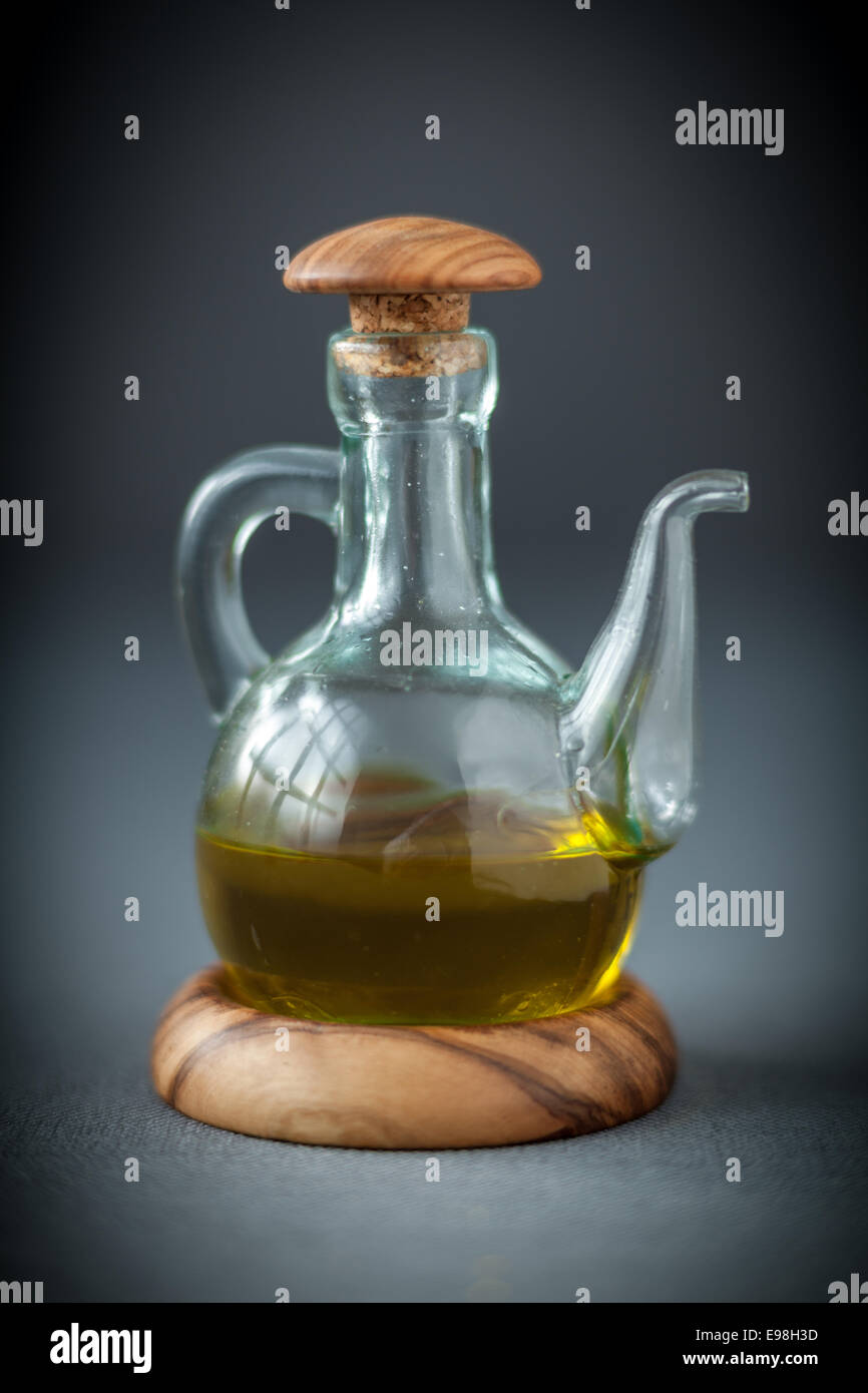 Transparentes Glas Karaffe mit einem hölzernen Stopfen Hälfte gefüllt mit gesunden Olivenöl als Dressing für Salate oder Kochzutat auf grau verwenden Stockfoto