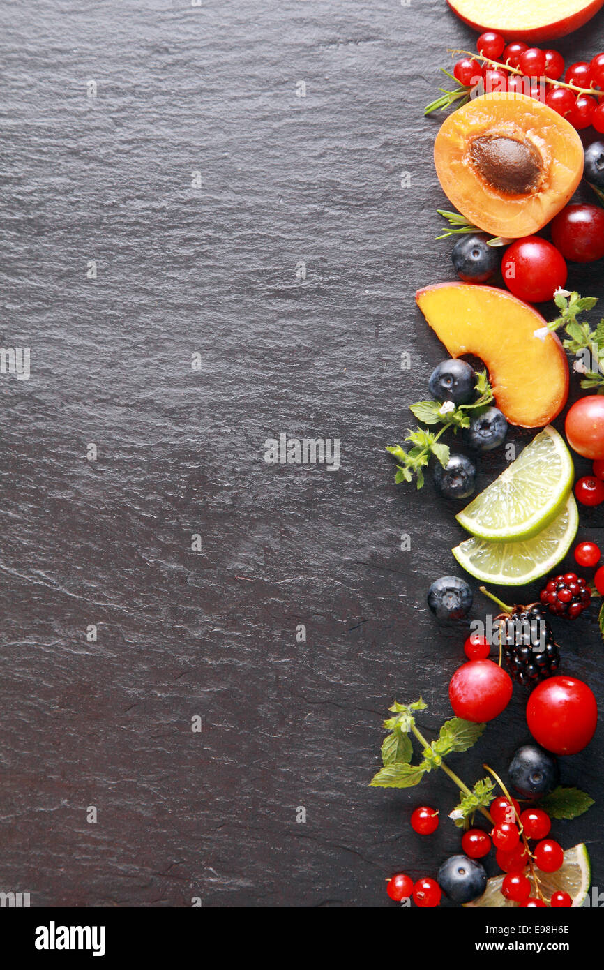 Grenze von frischem Obst und Kräuter auf der rechten Seite des Rahmens mit gemischte Beeren, Aprikose, Pfirsich und Zitrone auf einem dunklen grauen Schiefer Hintergrund mit Exemplar Stockfoto