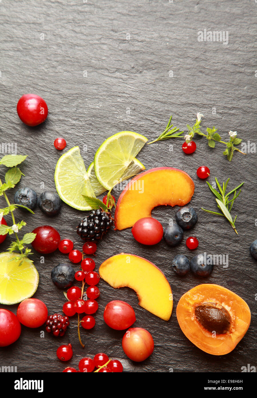 Bunte gesunde geschnittenes frisches Obst, verschiedene Beeren und Kräutern auf einen strukturierten dunklen grauen Schiefer Hintergrund mit Exemplar, Ansicht von oben Stockfoto