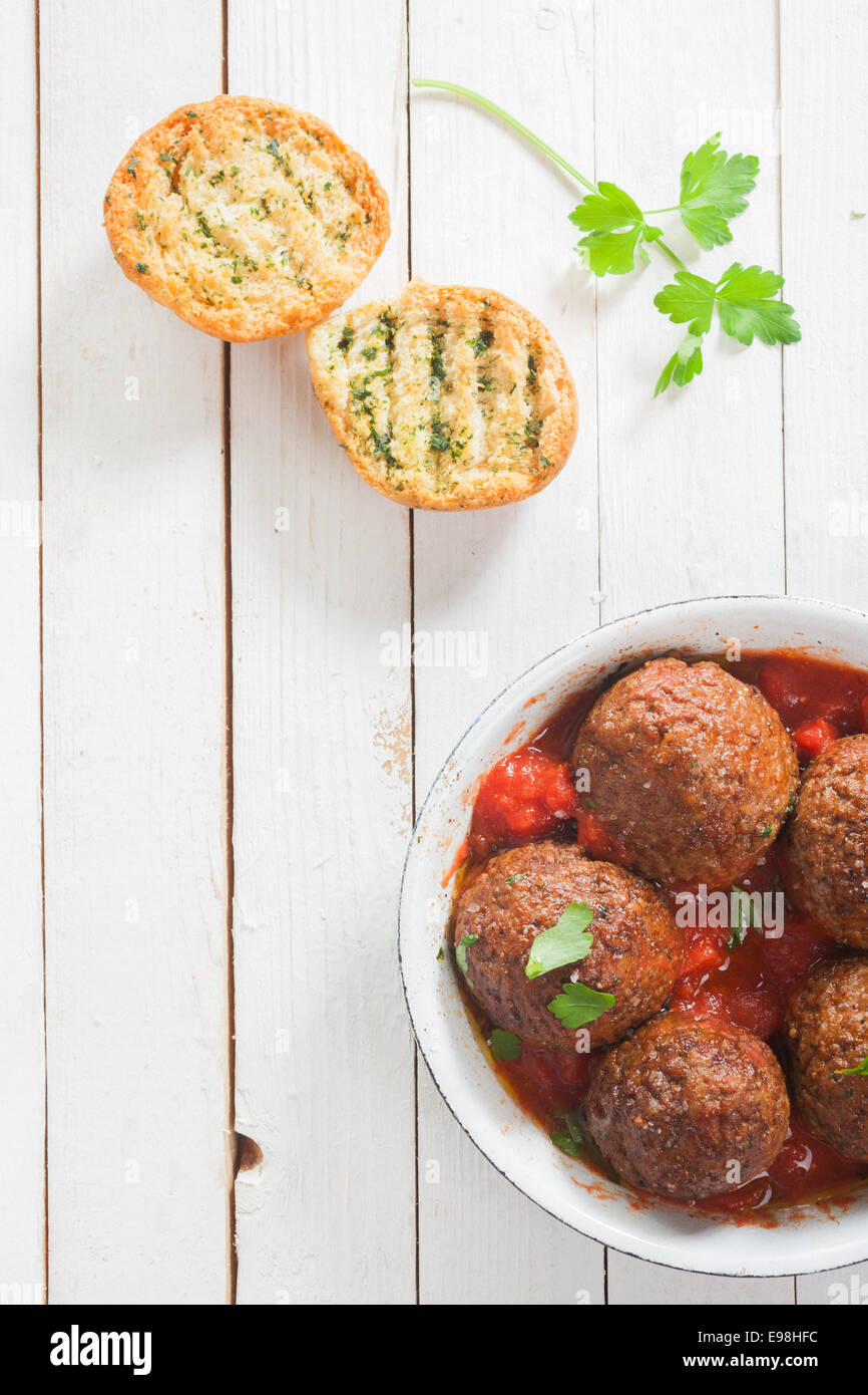 Pikante Rindfleisch Frikadellen in einer würzigen Tomatensauce mit frischen Kräutern, serviert in einem Topf mit knusprig goldene gegrillte Kräuter Brot und frischer Petersilie auf einem weißen hölzernen Tisch, Ansicht von oben Stockfoto