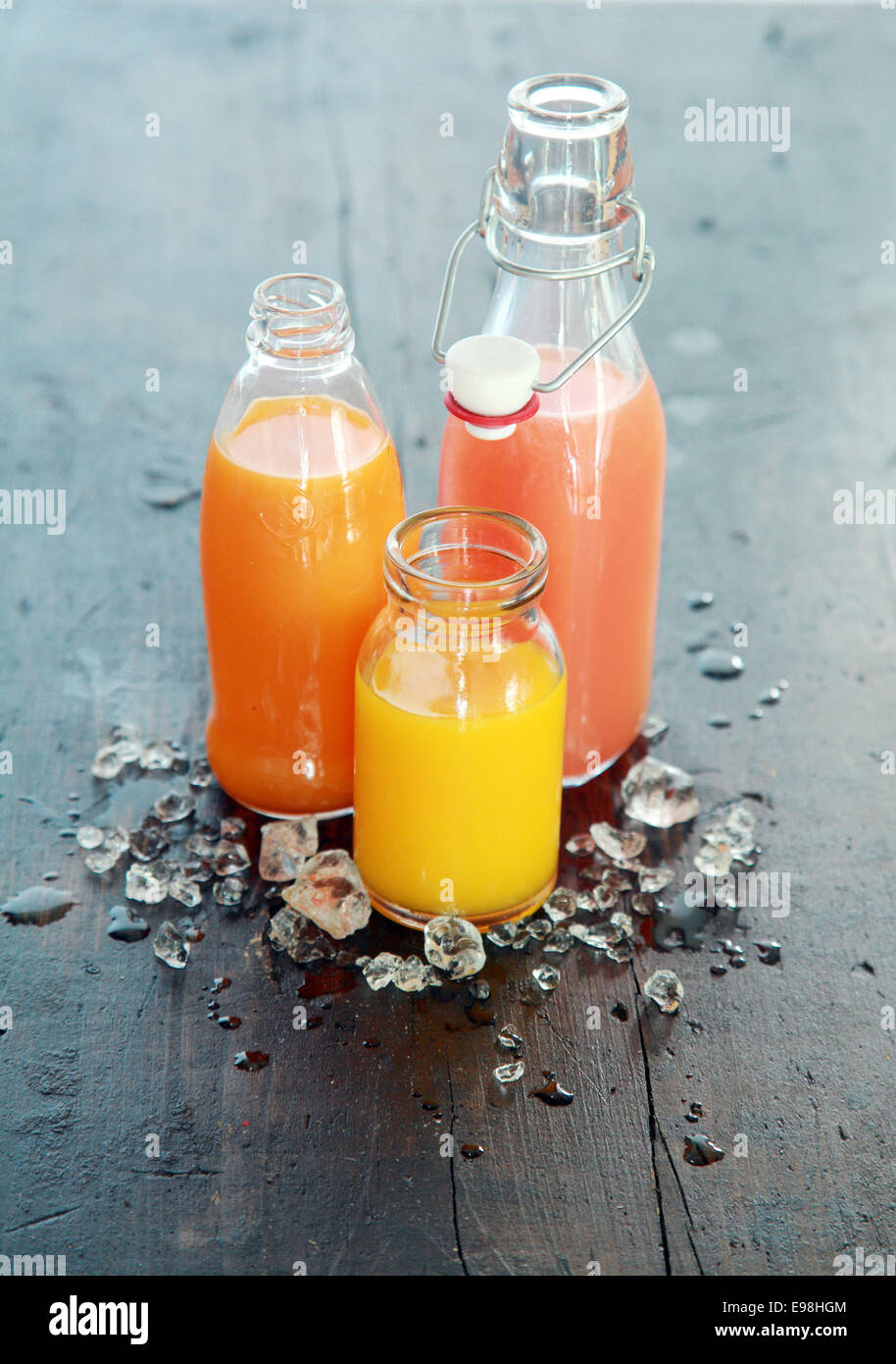 Gesunde frische hausgemachte Fruchtsäfte in Glasflaschen und Gläser mit Eis auf einem dunklen Tisch im Freien im Garten stehend gekühlt Stockfoto